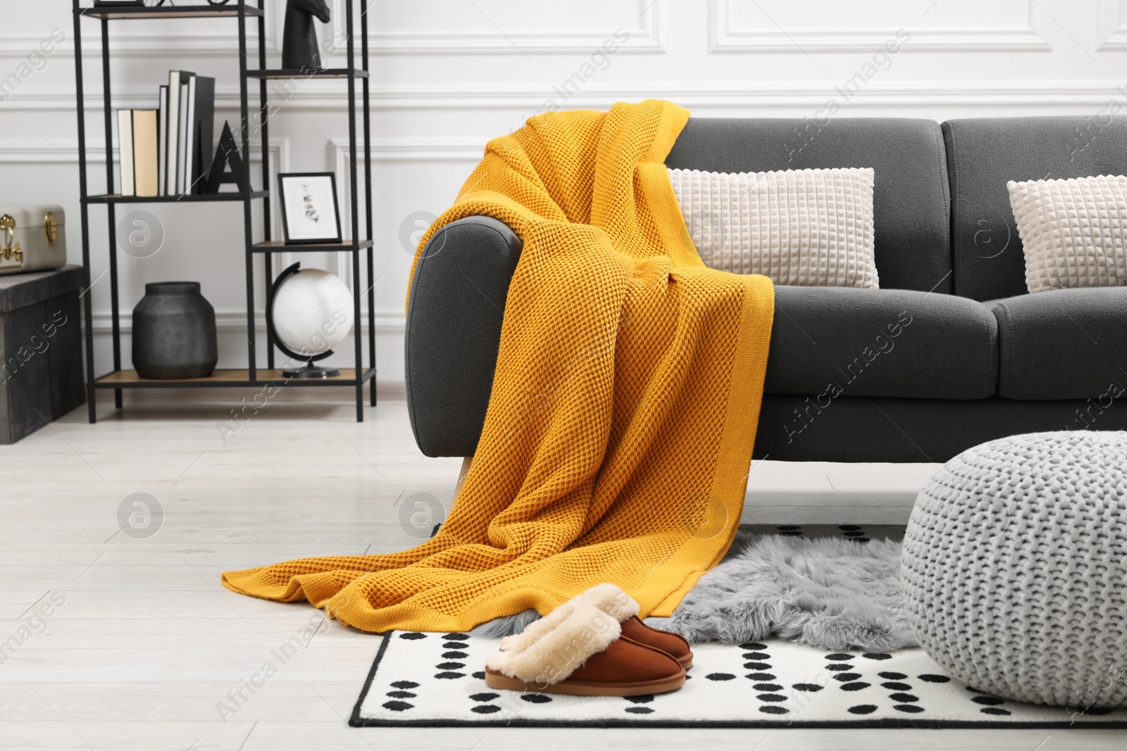 Photo of Stylish living room interior with comfortable sofa, orange blanket, slippers and ottoman