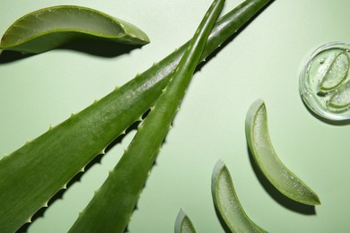 Photo of Cut aloe vera leaves and cosmetic gel on light green background, flat lay