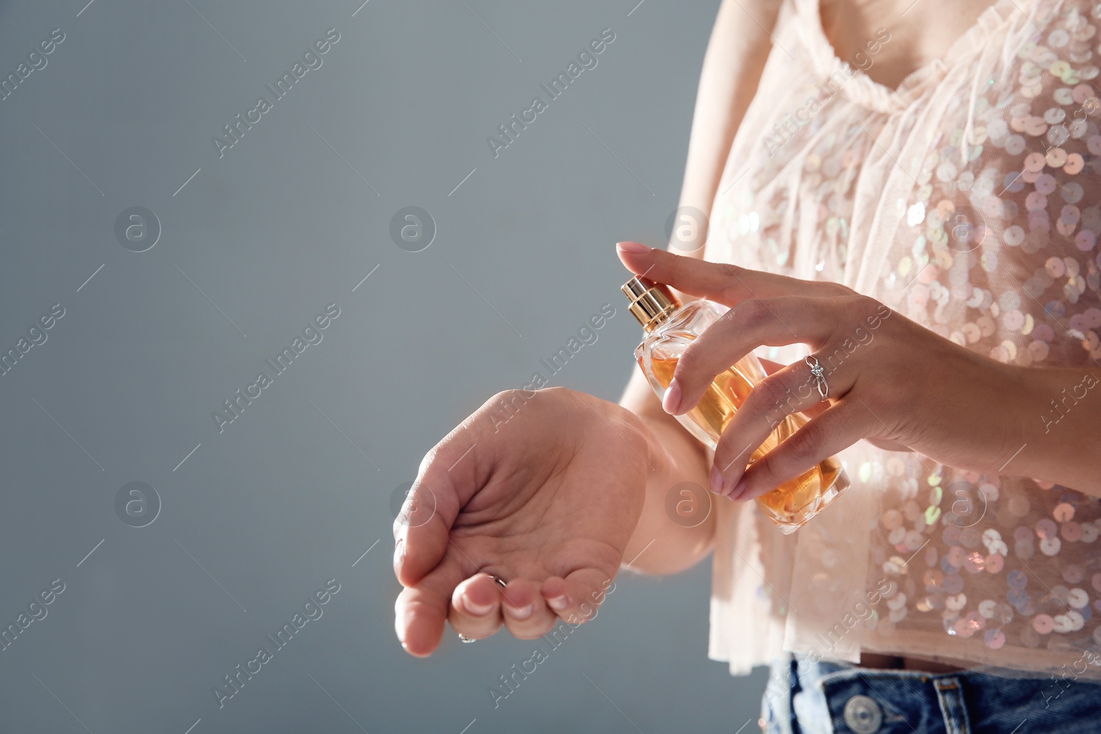 Photo of Young woman using perfume on gray background, closeup. Space for text