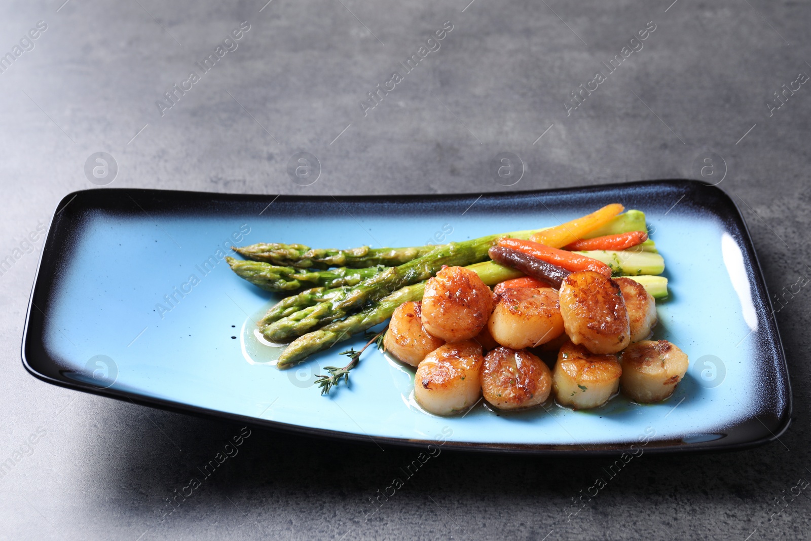 Photo of Delicious fried scallops with asparagus and vegetables on grey table