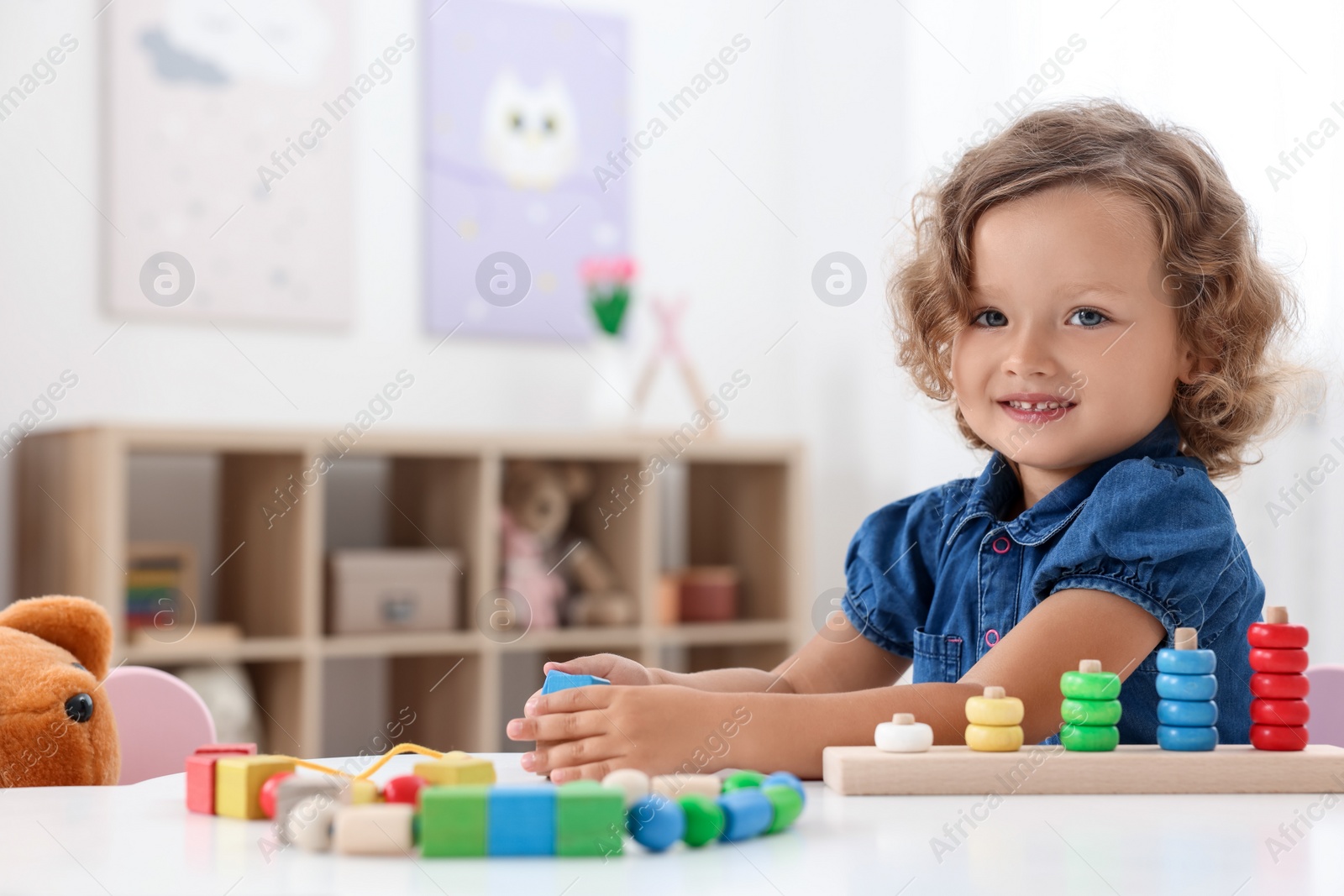 Photo of Motor skills development. Little girl playing with stacking and counting game at table indoors