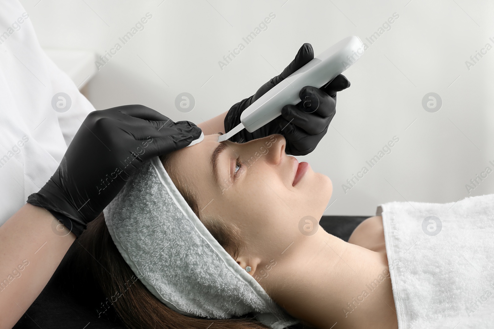 Photo of Cosmetologist using ultrasonic scrubber, closeup. Client having cleansing procedure in clinic