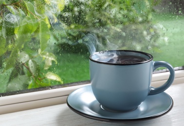 Cup of hot drink on windowsill. Rainy weather