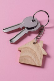Metallic keys with wooden keychain in shape of house on pink background