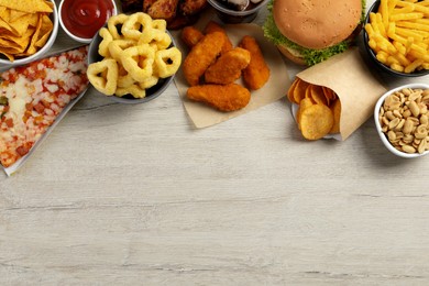 Photo of French fries, chicken nuggets and other fast food on white wooden table, flat lay with space for text