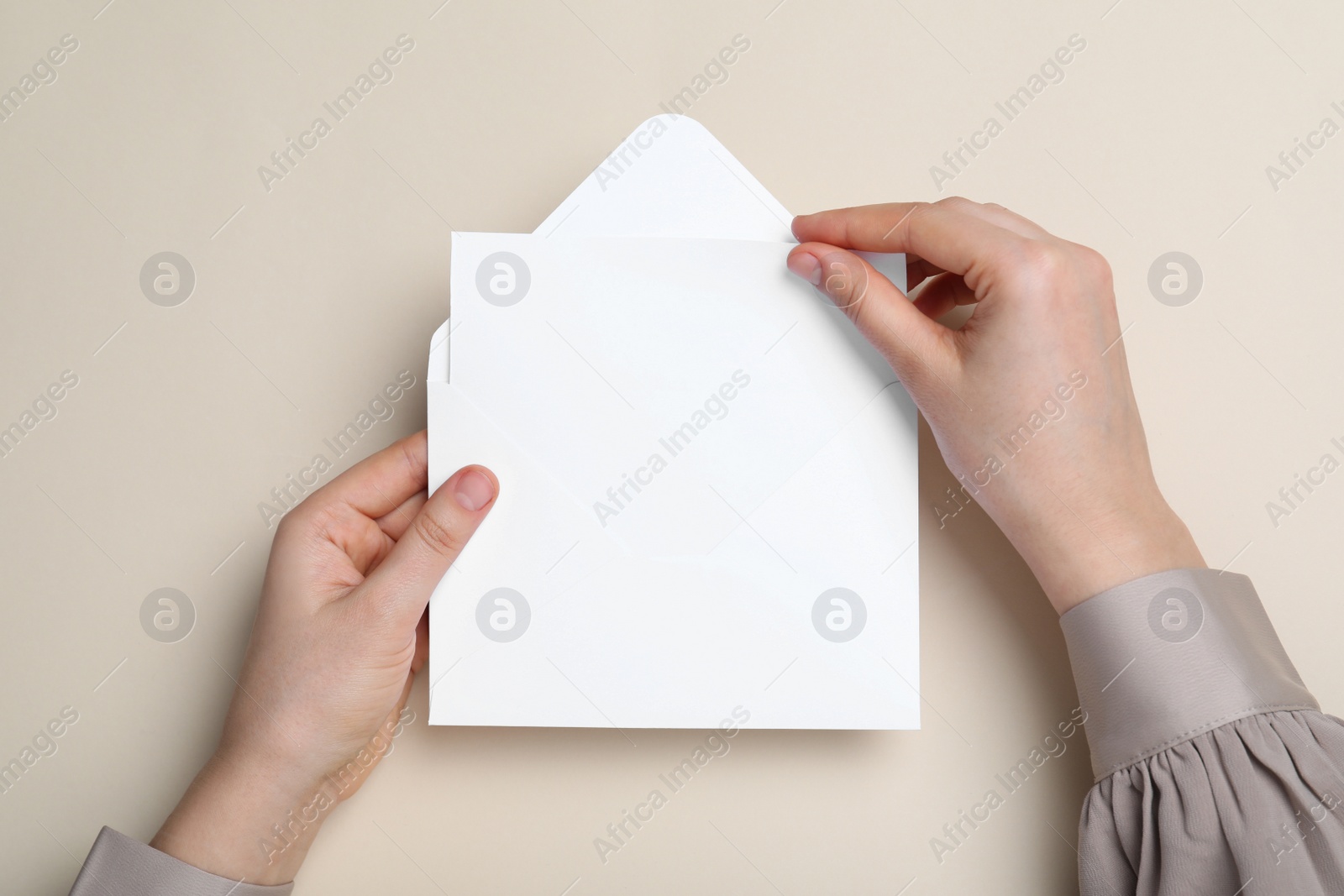 Photo of Woman taking card out of envelope on beige background, top view