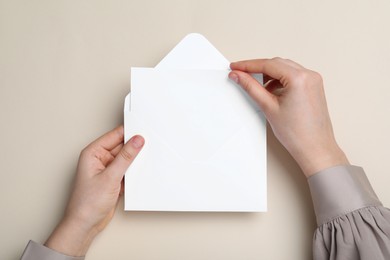 Photo of Woman taking card out of envelope on beige background, top view