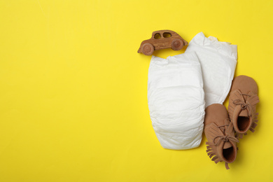 Diapers, toy car and child's shoes on yellow background, flat lay. Space for text