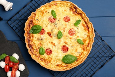 Photo of Delicious quiche with mozzarella cheese, tomatoes and basil on blue wooden table, flat lay