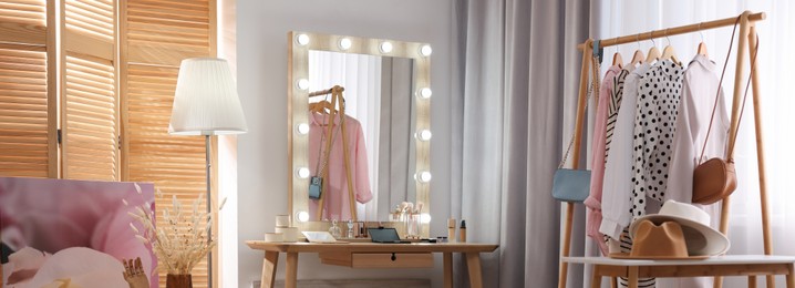 Image of Makeup room. Stylish dressing table with mirror, chair and clothing rack indoors, banner design