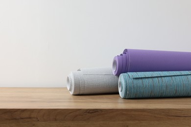 Three different wallpaper rolls on wooden table, space for text