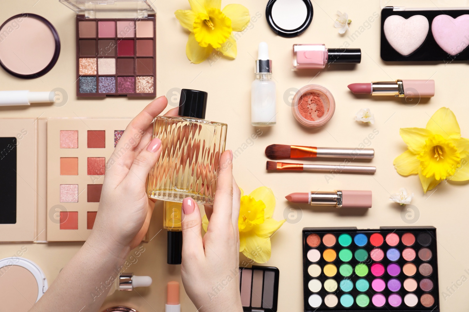 Photo of Woman with bottle of perfume, other different makeup products and beautiful spring flowers on beige background, top view