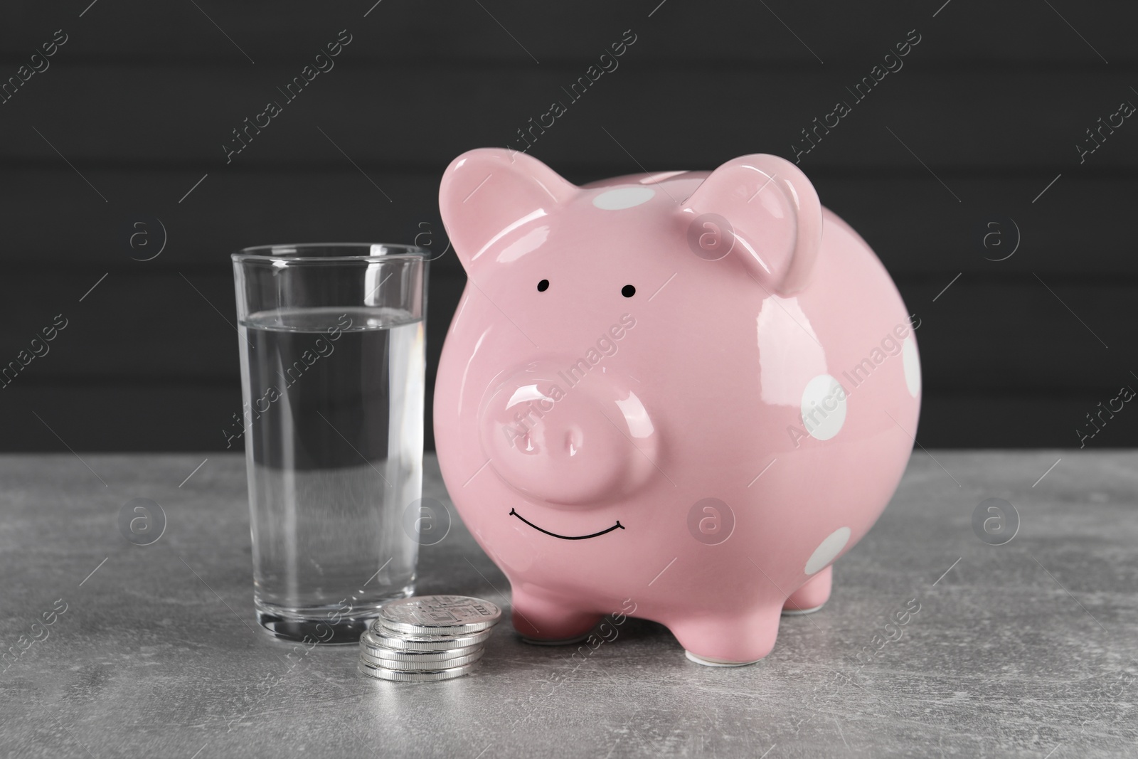 Photo of Water scarcity concept. Piggy bank, coins and glass of drink on grey table