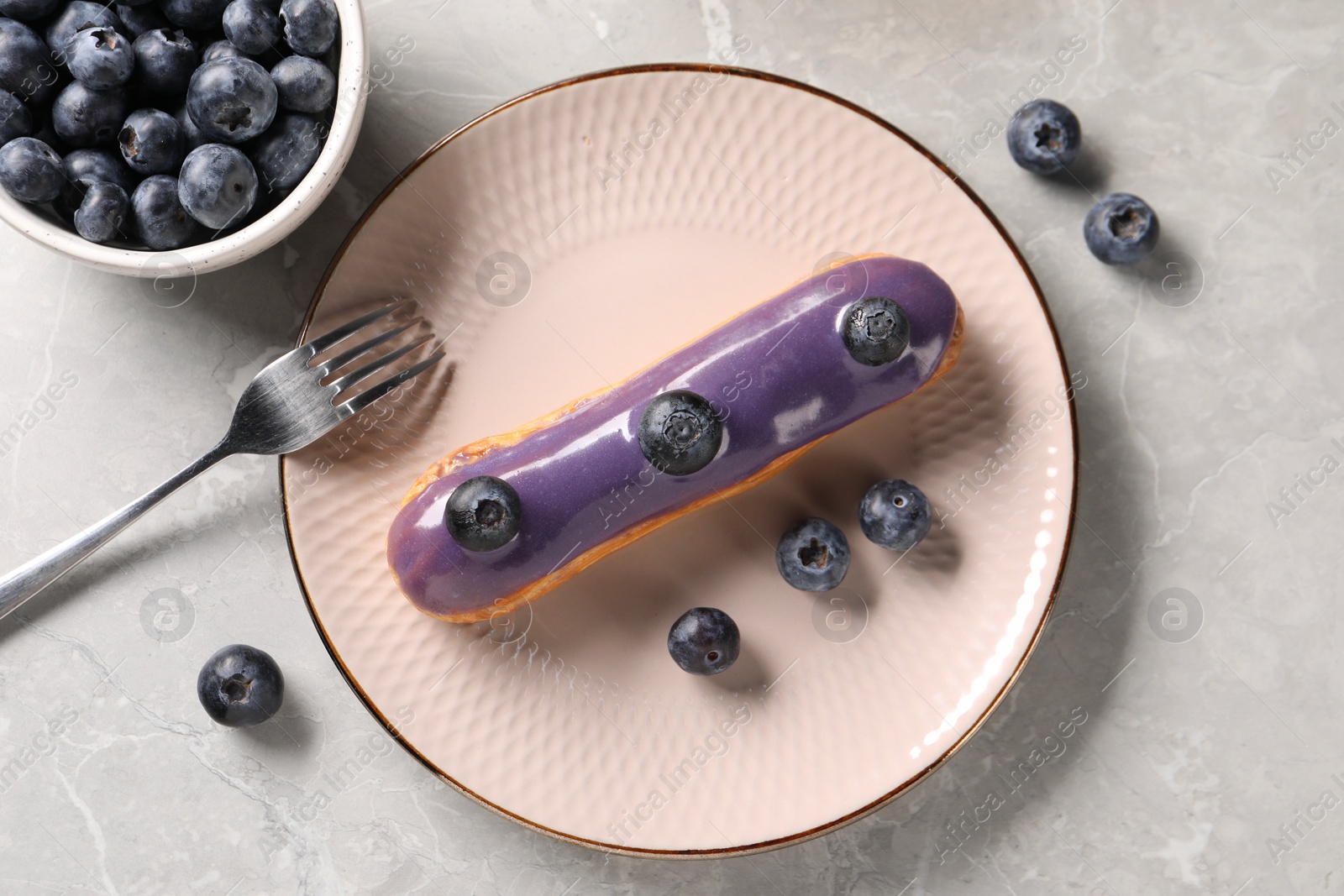 Photo of Tasty glazed eclair with blueberries on grey marble table, flat lay