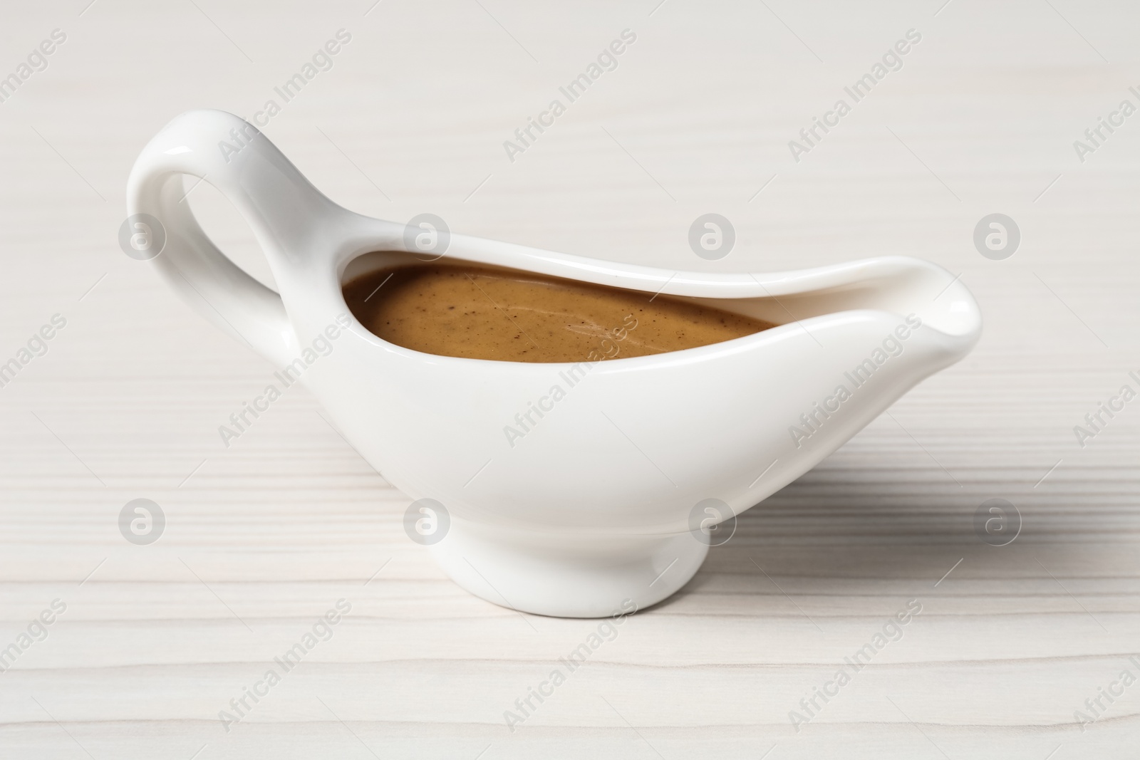 Photo of Delicious turkey gravy in sauce boat on white wooden table