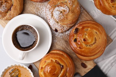 Photo of Delicious rolls with raisins, powdered sugar and coffee cup on table, flat lay. Sweet buns