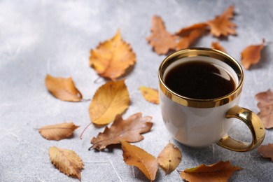 Photo of Composition with cup of hot drink and autumn leaves on light grey textured table. Space for text