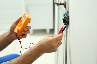 Professional electrician with tester checking light switch voltage indoors, closeup