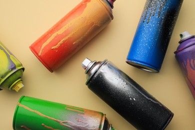 Photo of Used cans of spray paints on beige background, flat lay. Graffiti supplies