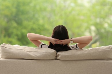 Teenage girl relaxing on sofa at home, back view