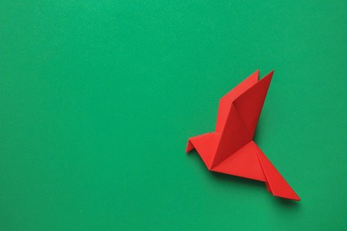Beautiful red origami bird on green background, top view. Space for text