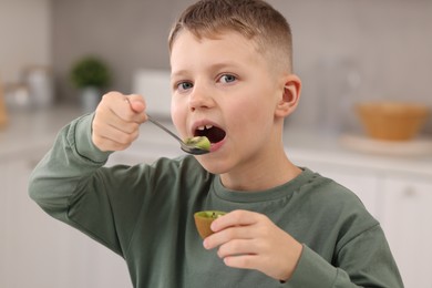 Photo of Cute boy eating tasty fresh kiwi indoors, closeup