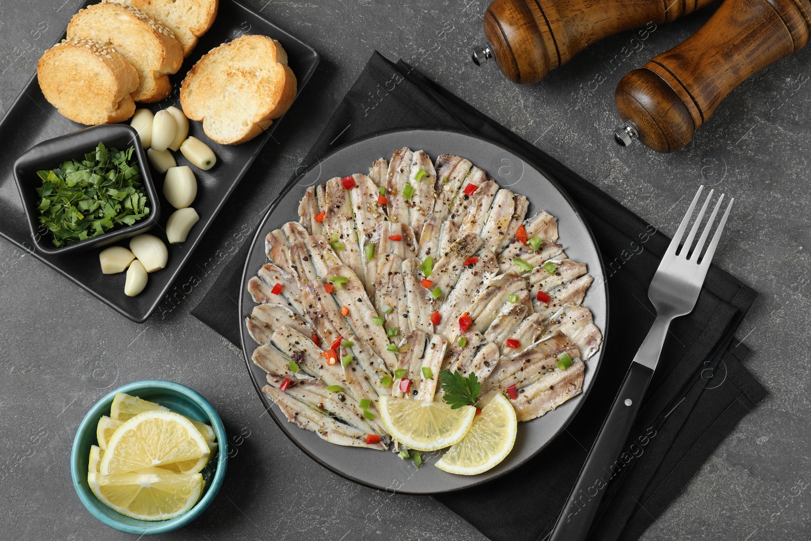 Photo of Tasty pickled anchovies served on grey textured table, flat lay