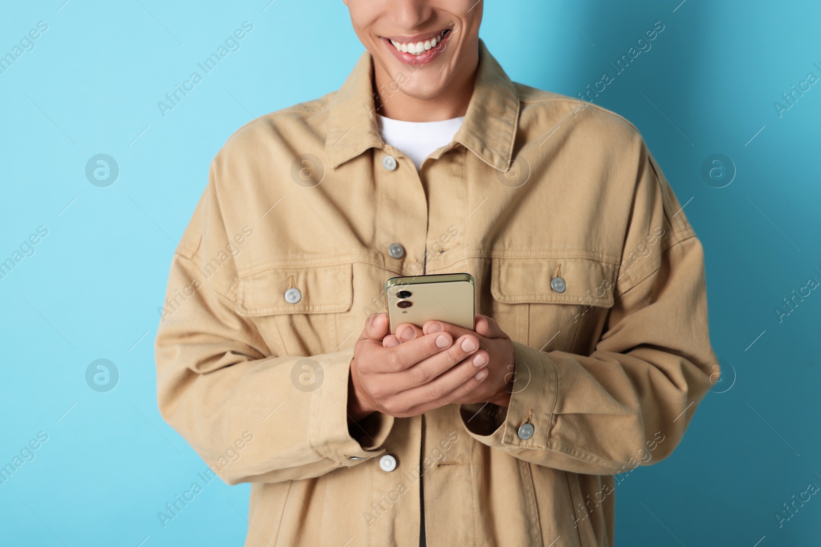 Photo of Young man sending message via smartphone on light blue background, closeup