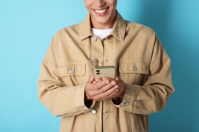 Young man sending message via smartphone on light blue background, closeup