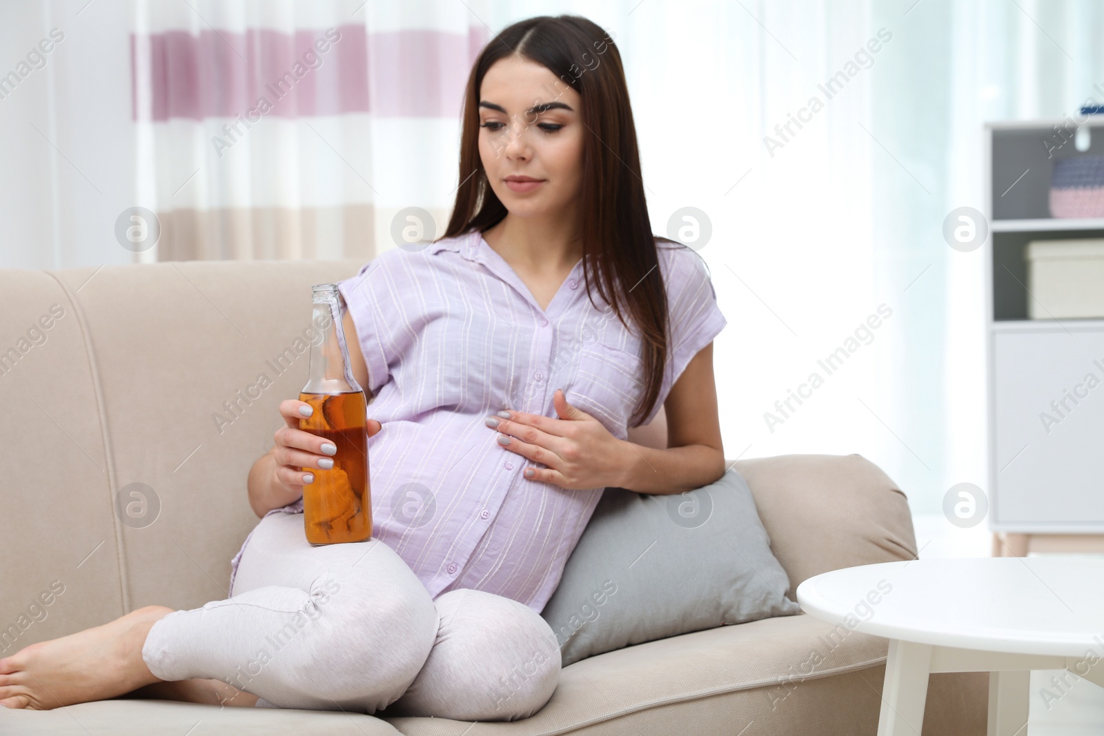 Photo of Future mother with bottle of beer at home. Alcohol abuse during pregnancy