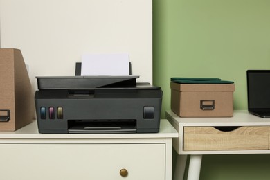Photo of Modern printer with paper on white chest of drawers near stylish workplace indoors