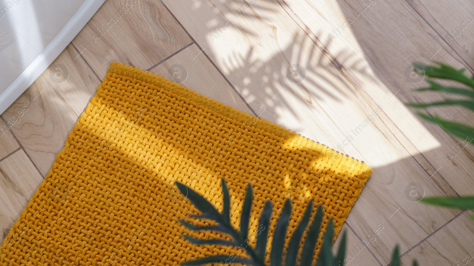 Photo of Soft mustard color bath mat on wooden floor in bathroom, above view