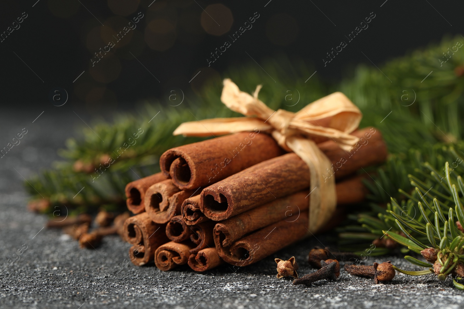 Photo of Different spices. Aromatic cinnamon sticks, clove seeds and fir branches on dark gray textured table, closeup