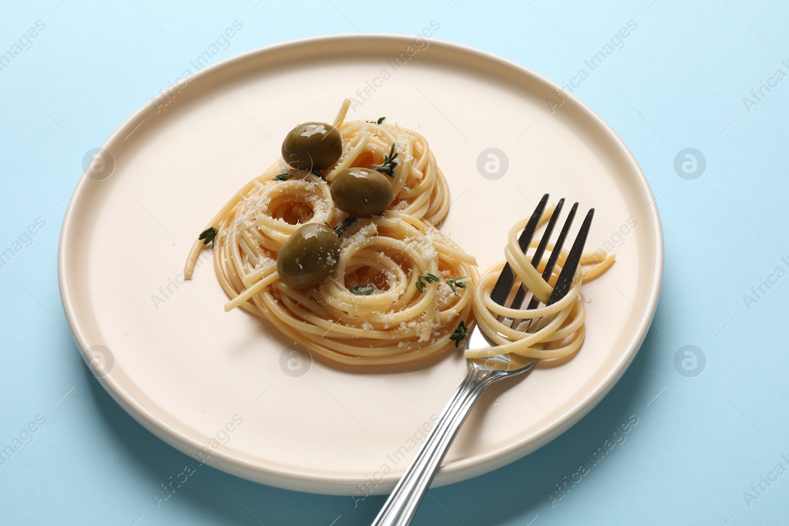 Photo of Heart made of tasty spaghetti, fork, olives and cheese on light blue background