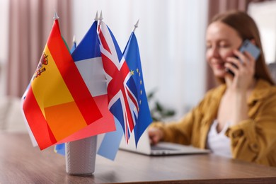 Photo of Woman talking on smartphone at table indoors, focus on different flags