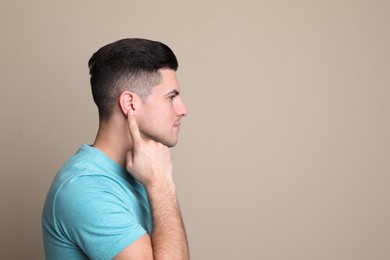 Photo of Man pointing at his ear on beige background. Space for text