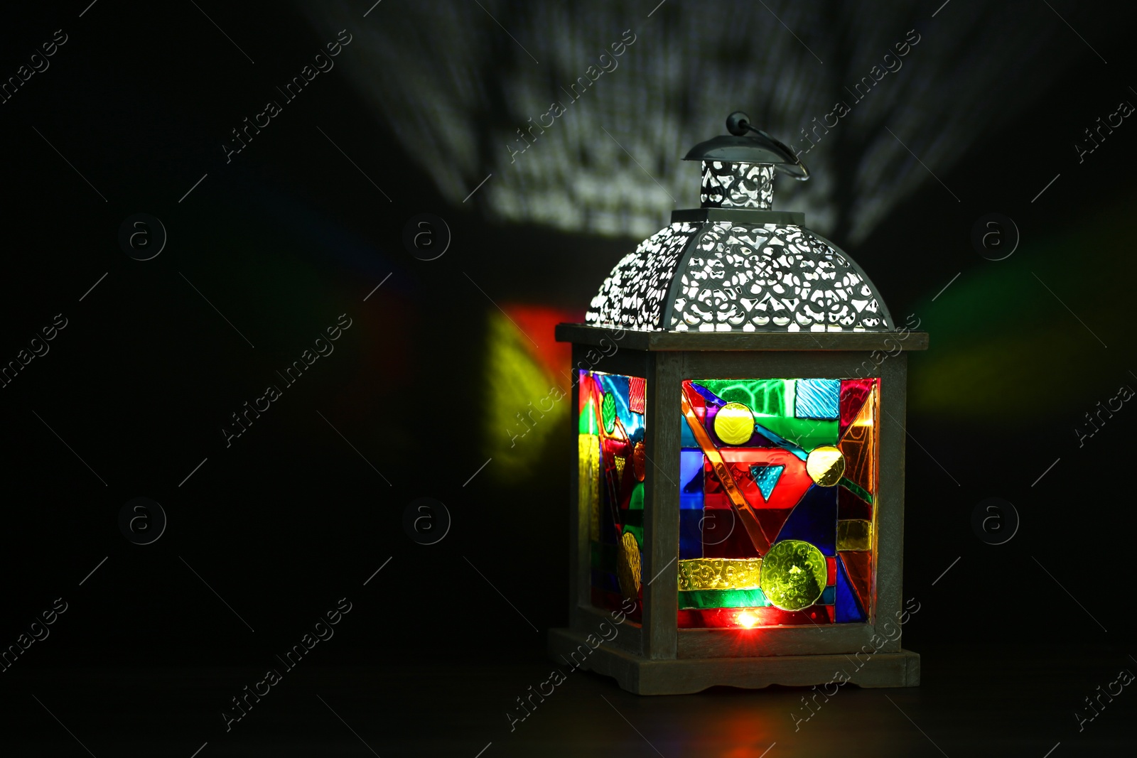 Photo of Decorative Arabic lantern on table against dark background. Space for text