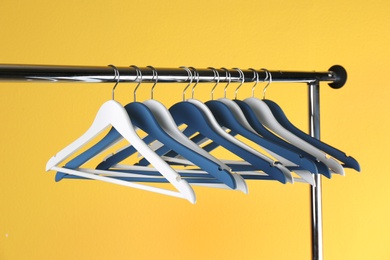 Metal rack with clothes hangers on color background