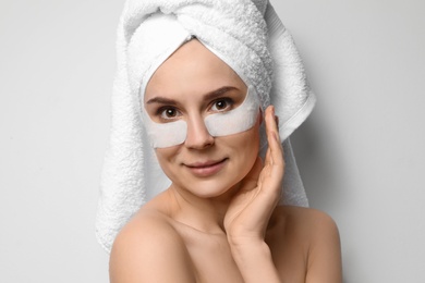 Photo of Beautiful woman with eye patches against light background. Facial mask