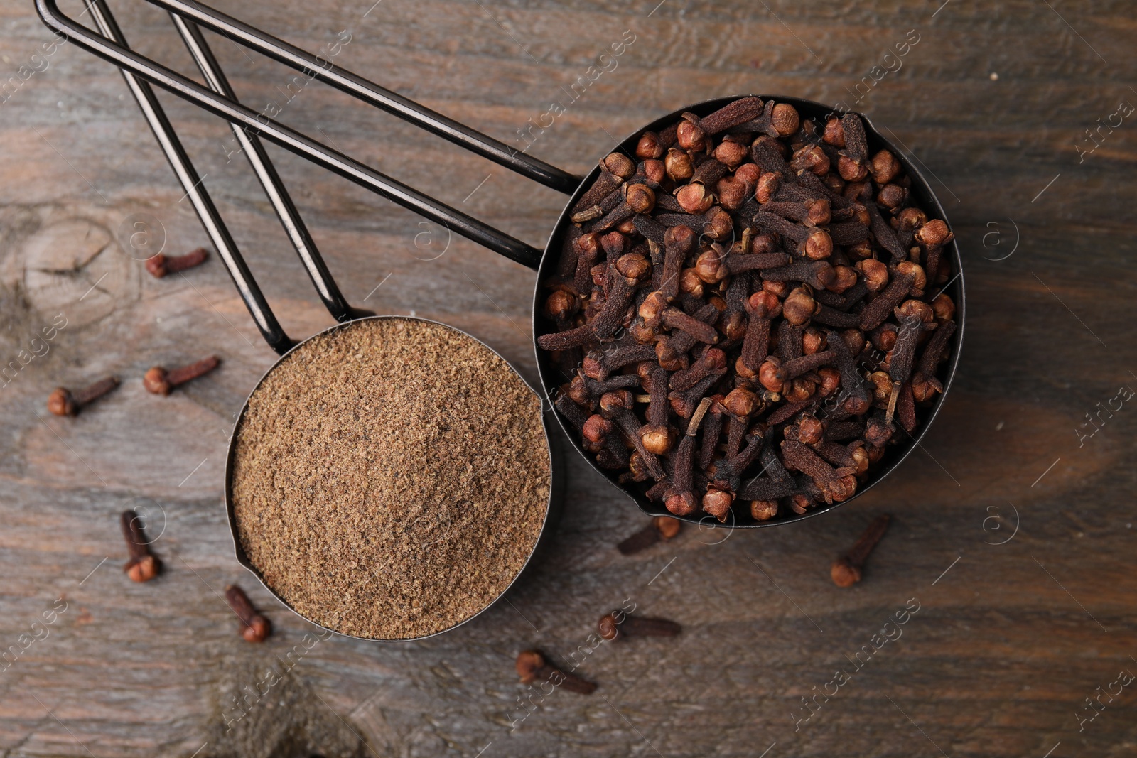 Photo of Aromatic clove powder and dried buds in scoops on wooden table, top view