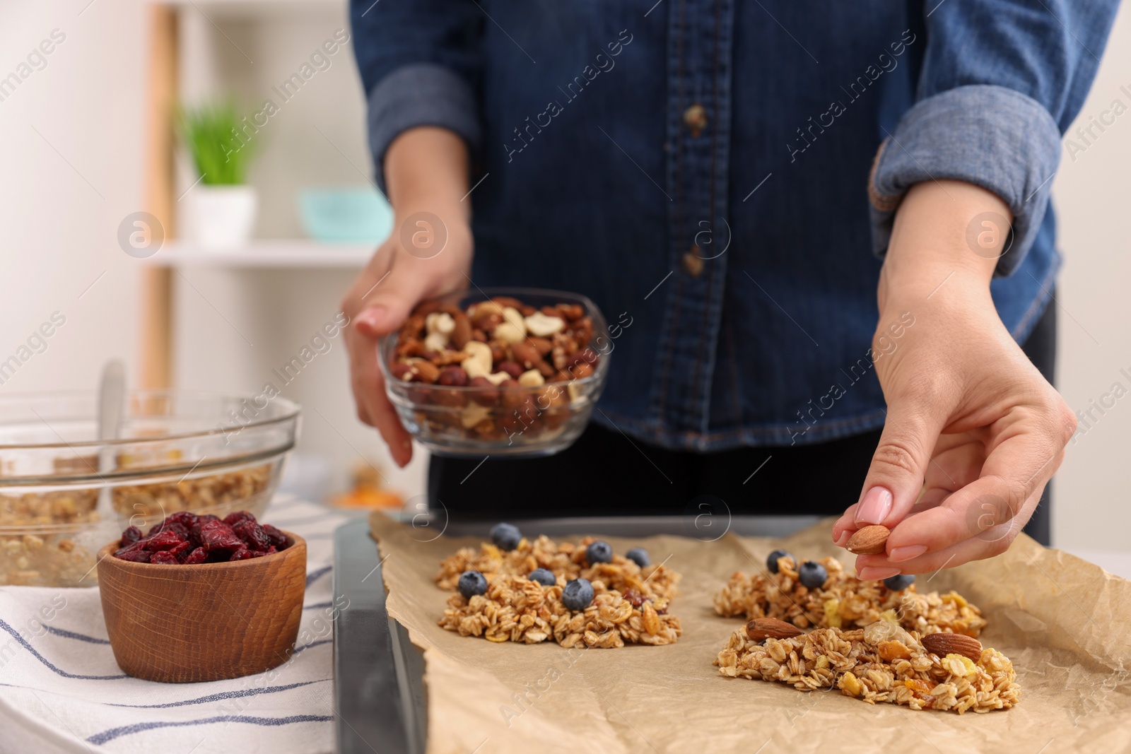 Photo of Making granola bars. Woman with nuts at table in kitchen, closeup