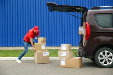 Photo of Courier loading packages in car trunk outdoors