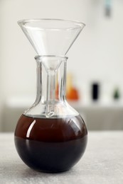 Photo of Flask with brown crude oil and filter funnel on light grey table