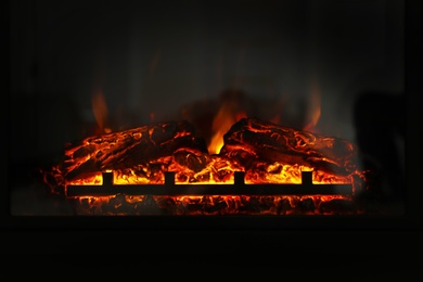 Photo of Firewood burning bright in elegant fireplace indoors, closeup