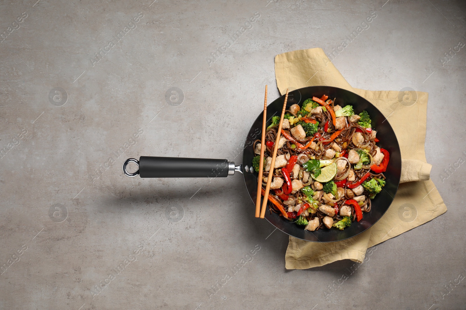 Photo of Stir-fry. Tasty noodles with meat in wok and chopsticks on grey textured table, top view