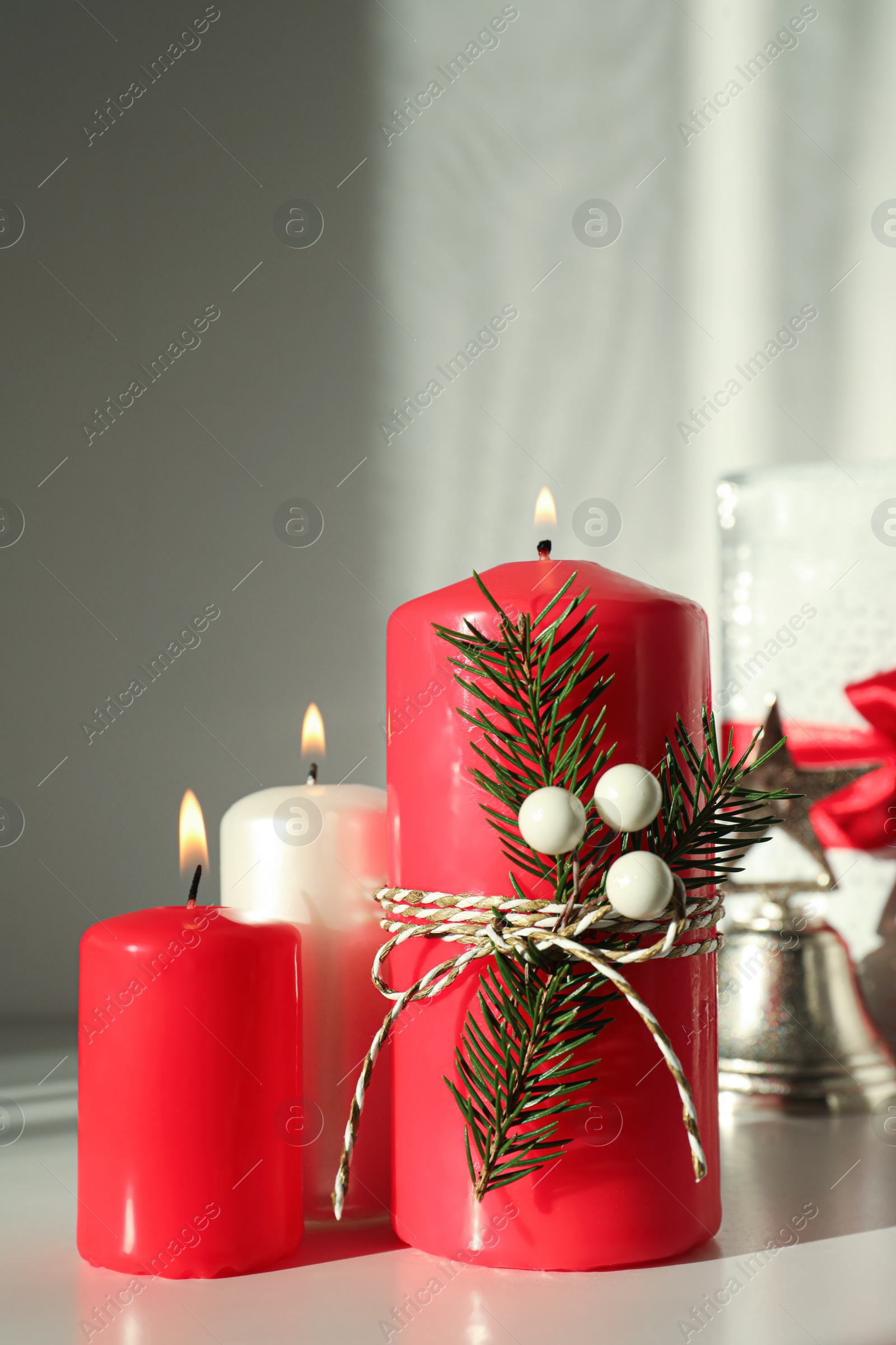 Photo of Burning candles with Christmas decor on white table