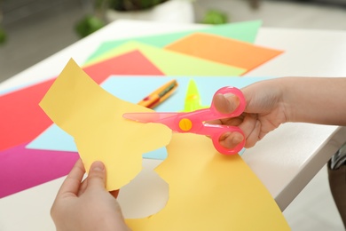 Photo of Child cutting out paper heart with plastic scissors at table, closeup