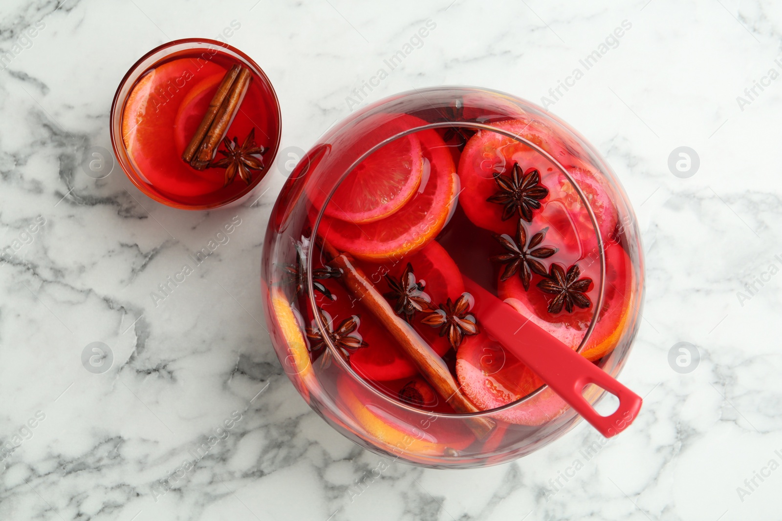 Photo of Glass and bowl of delicious aromatic punch drink on white marble table, flat lay