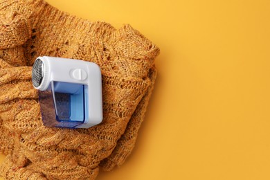 Photo of Modern fabric shaver and knitted sweater on orange background, top view. Space for text