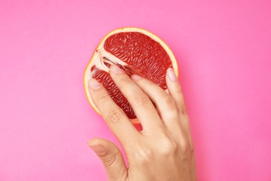 Photo of Young woman touching half of grapefruit on pink background, top view. Sex concept